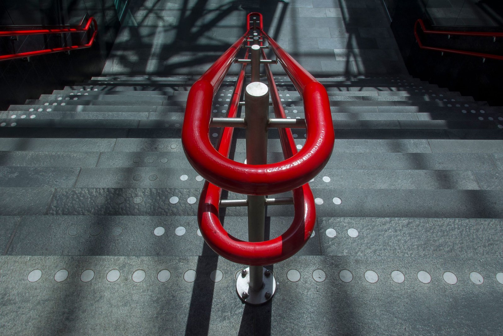 A striking image of a modern staircase with a vibrant red handrail in an urban setting.