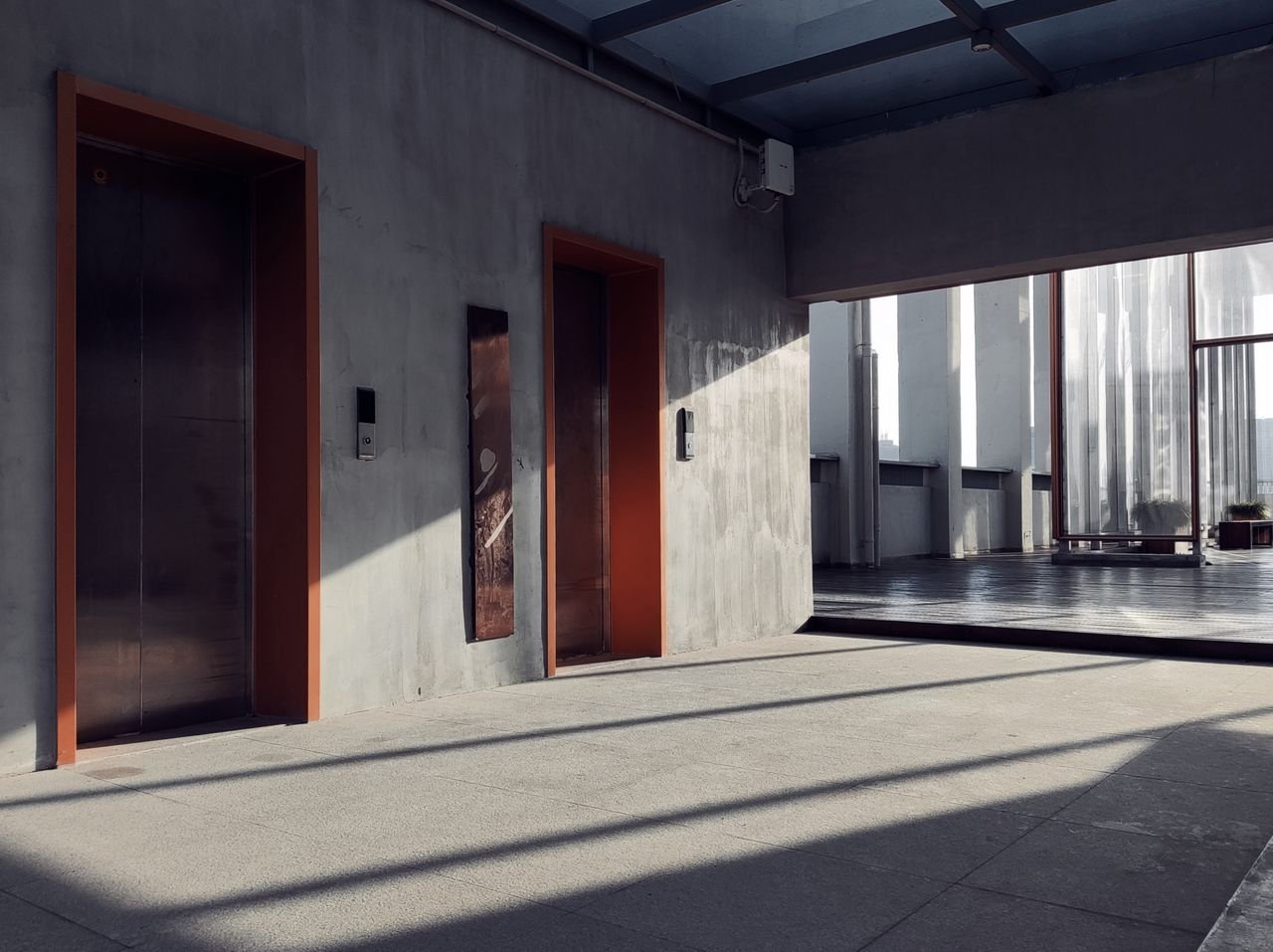 A minimalist interior showcasing elevators, sunlight, and striking shadows in a modern hallway.